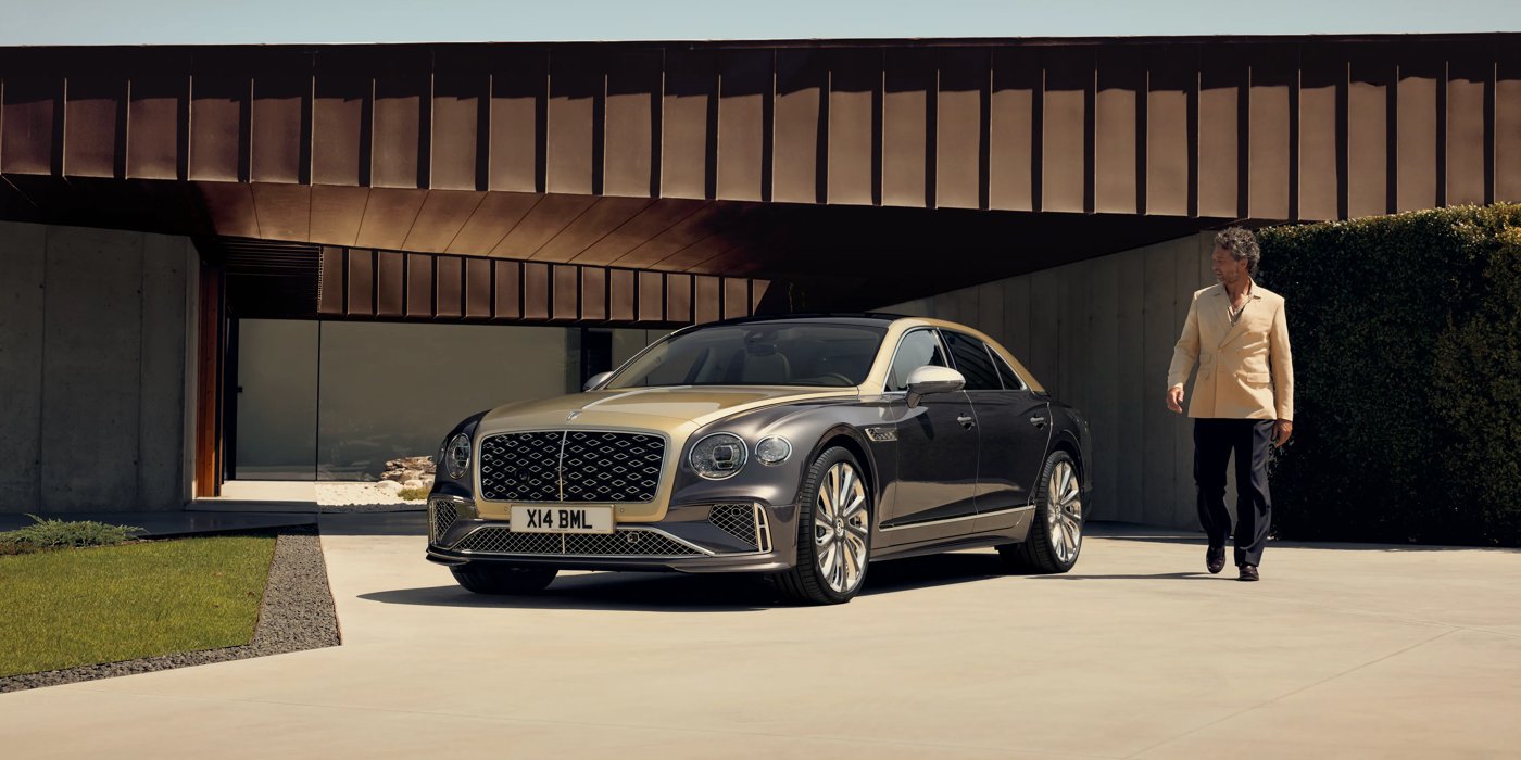 Bentley St Peter Bentley New Flying Spur Mulliner V8 hybrid sedan front three quarters in Rose Gold over Magnetic paint, parked near modern home