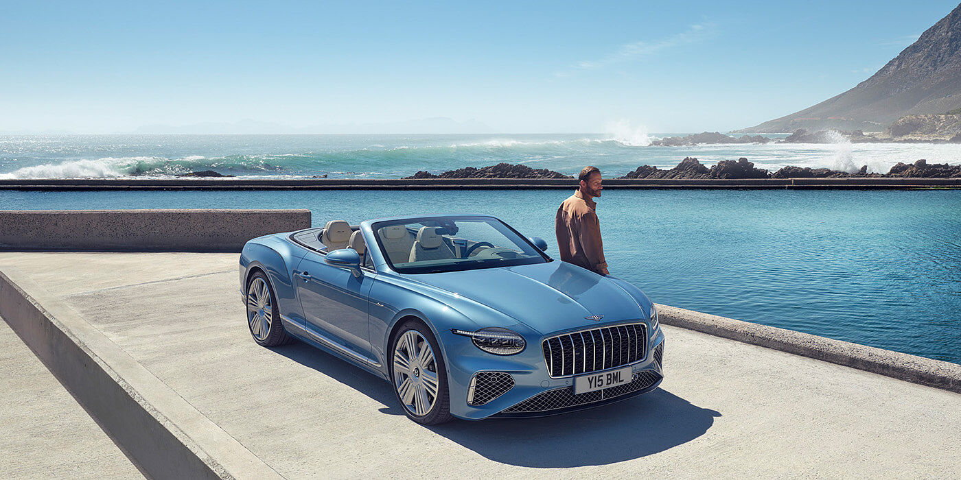 Bentley St Peter New Bentley Continental GTC Azure convertible front view in Light Windsor blue paint with 22 inch ten spoke wheels parked by the sea in the sunshine