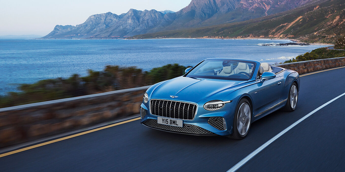 Bentley St Peter New Bentley Continental GTC Azure convertible in Light Windsor blue paint with 22 inch Azure wheels and chrome grill, driving dynamically by the sea