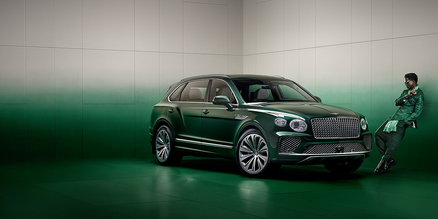 Bentley St Peter Wisdom K leans against wall next to Bentley Bentayga Extended Wheelbase Atelier Edition SUV in Light Emerald green paint