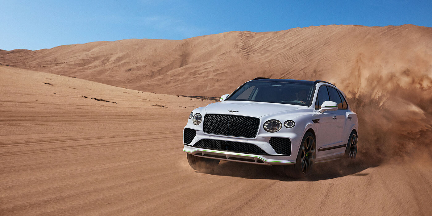 Bentley St Peter Bentley Bentayga Speed SUV front three quarter in Snow Quarts Pearlescent by Mulliner white paint driving dynamically through the desert