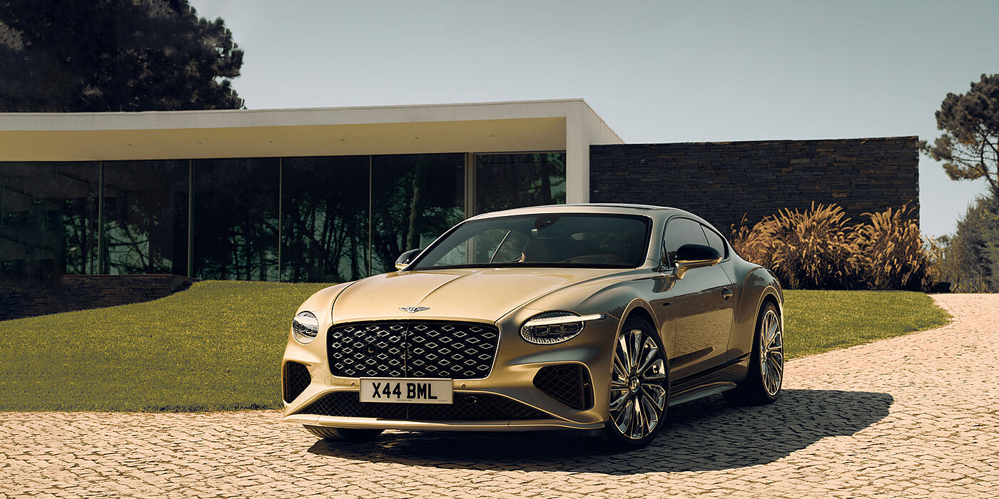 Bentley St Peter Bentley Continental GT Mulliner coupe front three quarters in Patina paint parked outside a glass fronted building with a grass lawn behind it