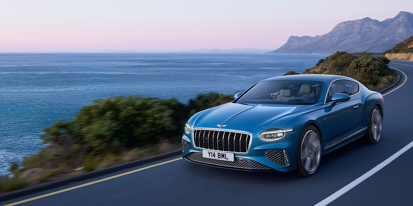 Bentley St Peter New Bentley Continental GT Azure coupe in Light Windsor blue paint with 22 inch Azure wheels and chrome grill, driving dynamically by the sea