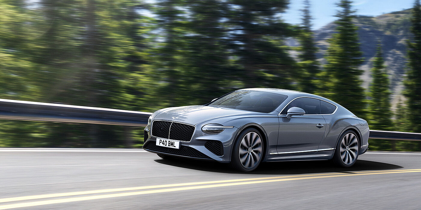 Bentley St Peter New Bentley Continental GT coupe in Silverlake paint and 22 inch ten-spoke wheels, driving dynamically on a tree-lined road in the sunshine